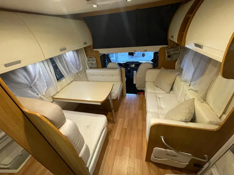 Rivestimento camper: interni in finta pelle chiara con dinette e divanetto, vista verso la cabina