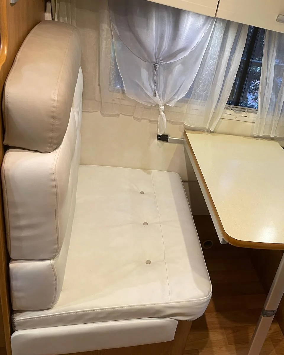 Rifacimento degli interni del camper: dinette a due panche di un camper non recente, con sedute e schienali rifatti in finta pelle bianca